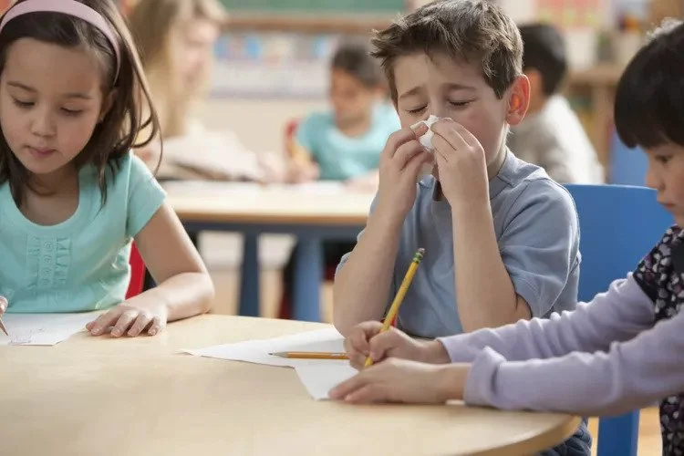 Niños en sala de clases dibujando y uno de ellos sonándose la nariz por estar resfriado