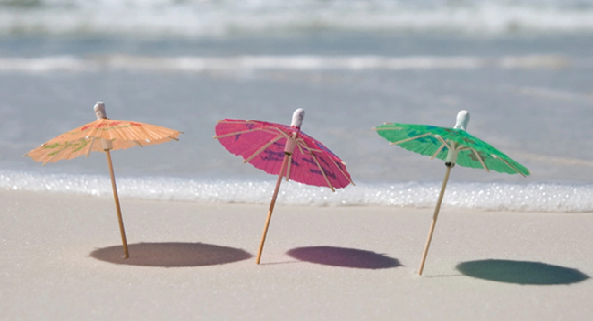 3 ombrelles en papier miniatures alignées sur une plage