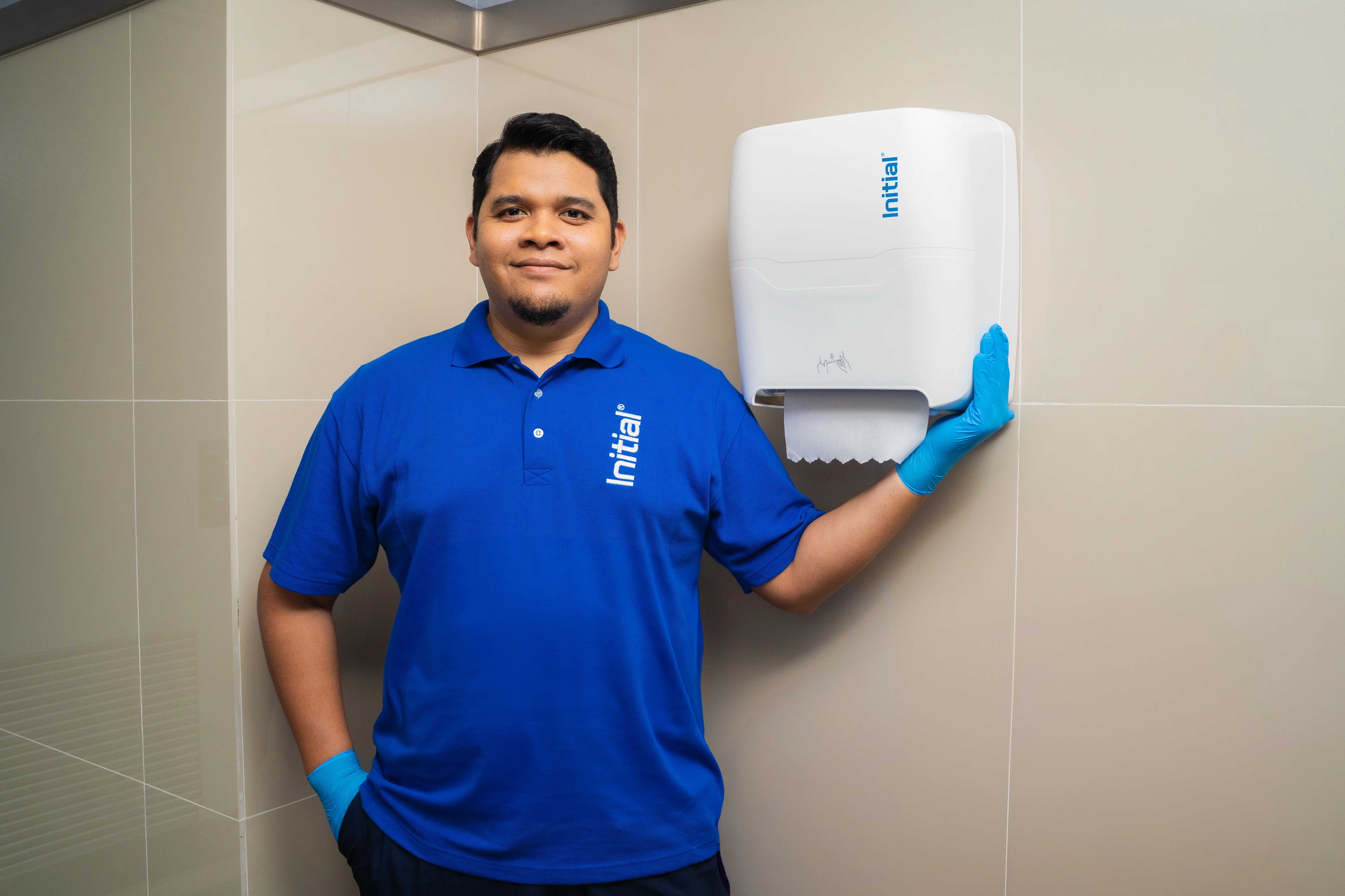 Técnio de Initial junto a un dispensador de papel toalla para baño de empresa