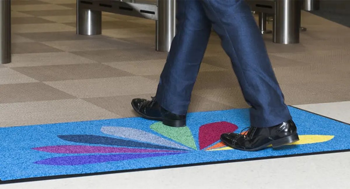 A visitor walking across a high-quality custom logo mat at a corporate entrance, showcasing professional brand identity and dust control.