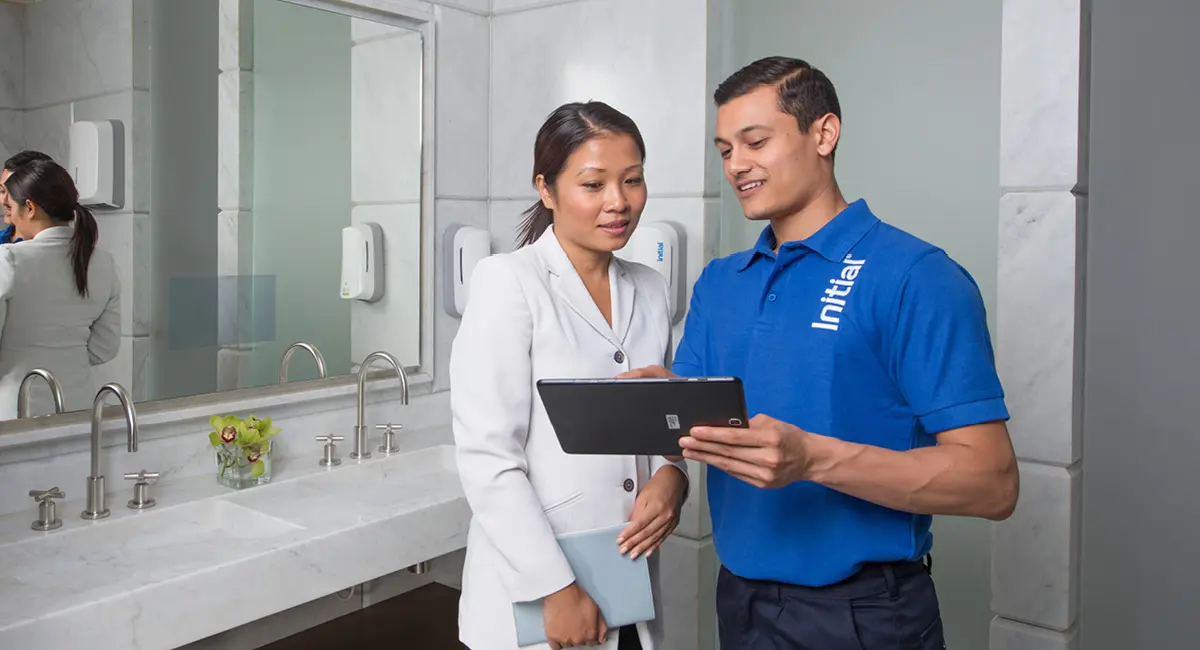 An Initial hygiene technician showing data on a tablet to a client in a modern restroom.